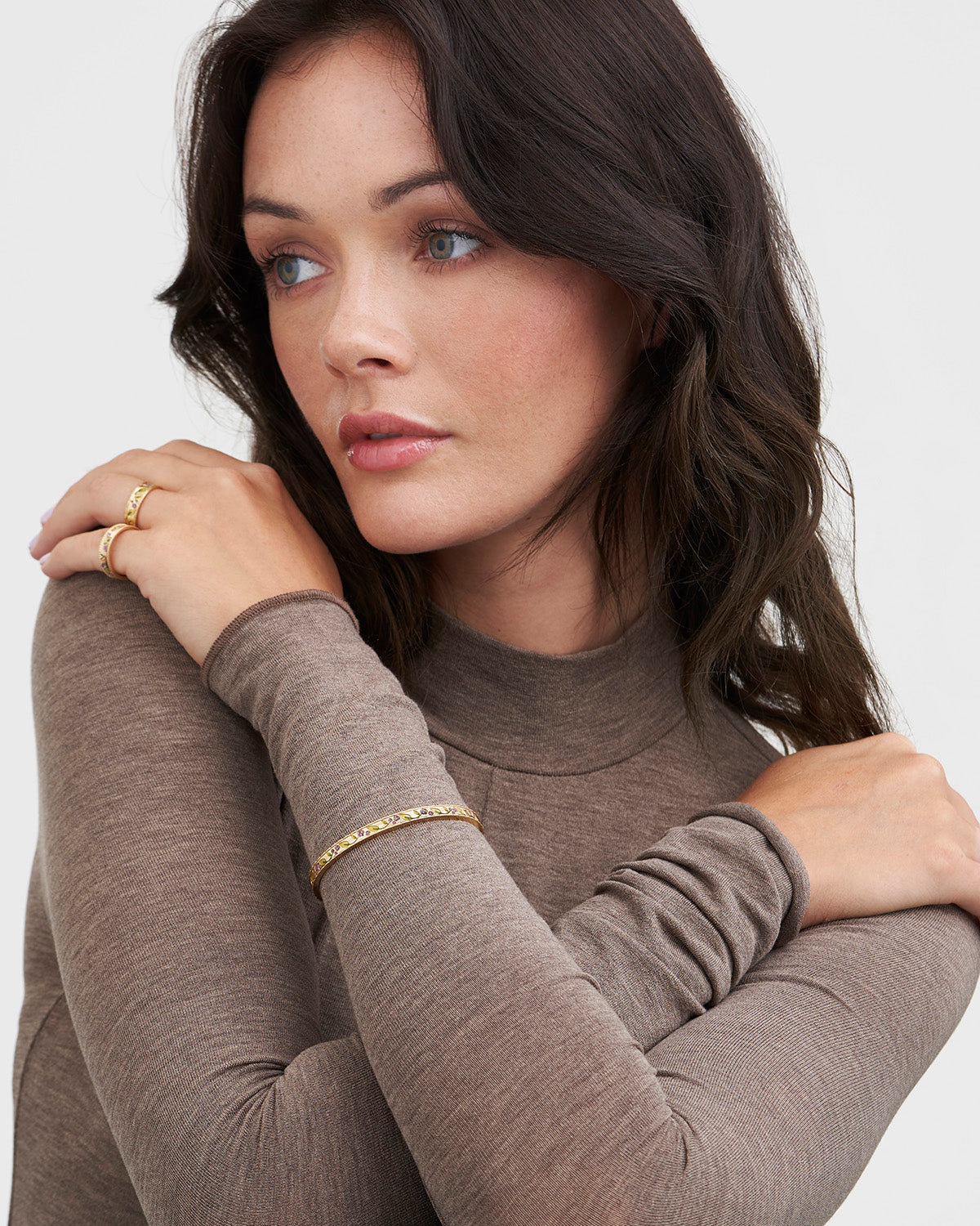 Woman wearing a brown turtleneck sweater with gold floral bangle on a white background