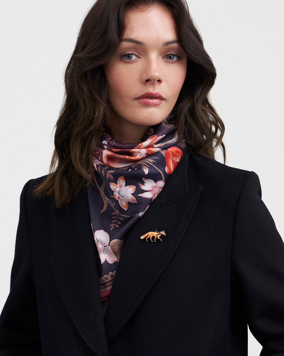 Woman wearing a black coat with a floral scarf and a brooch on a white background