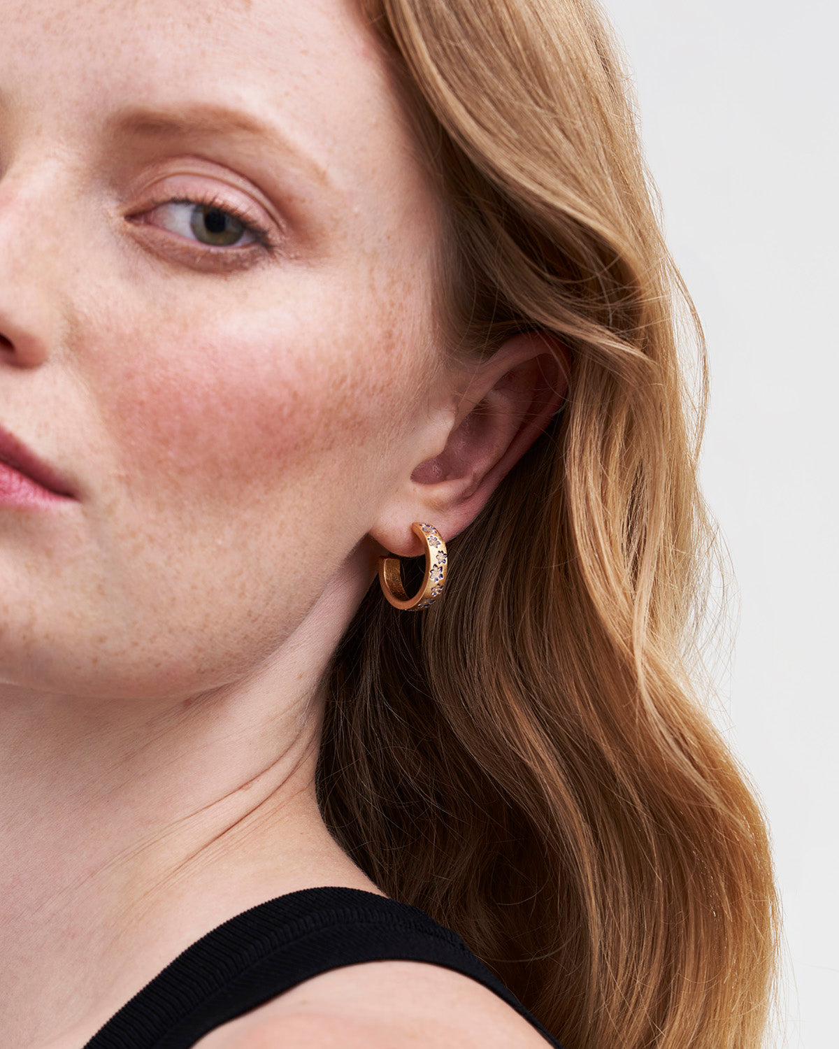 Close-up of a person wearing gold hoop earrings with a neutral background