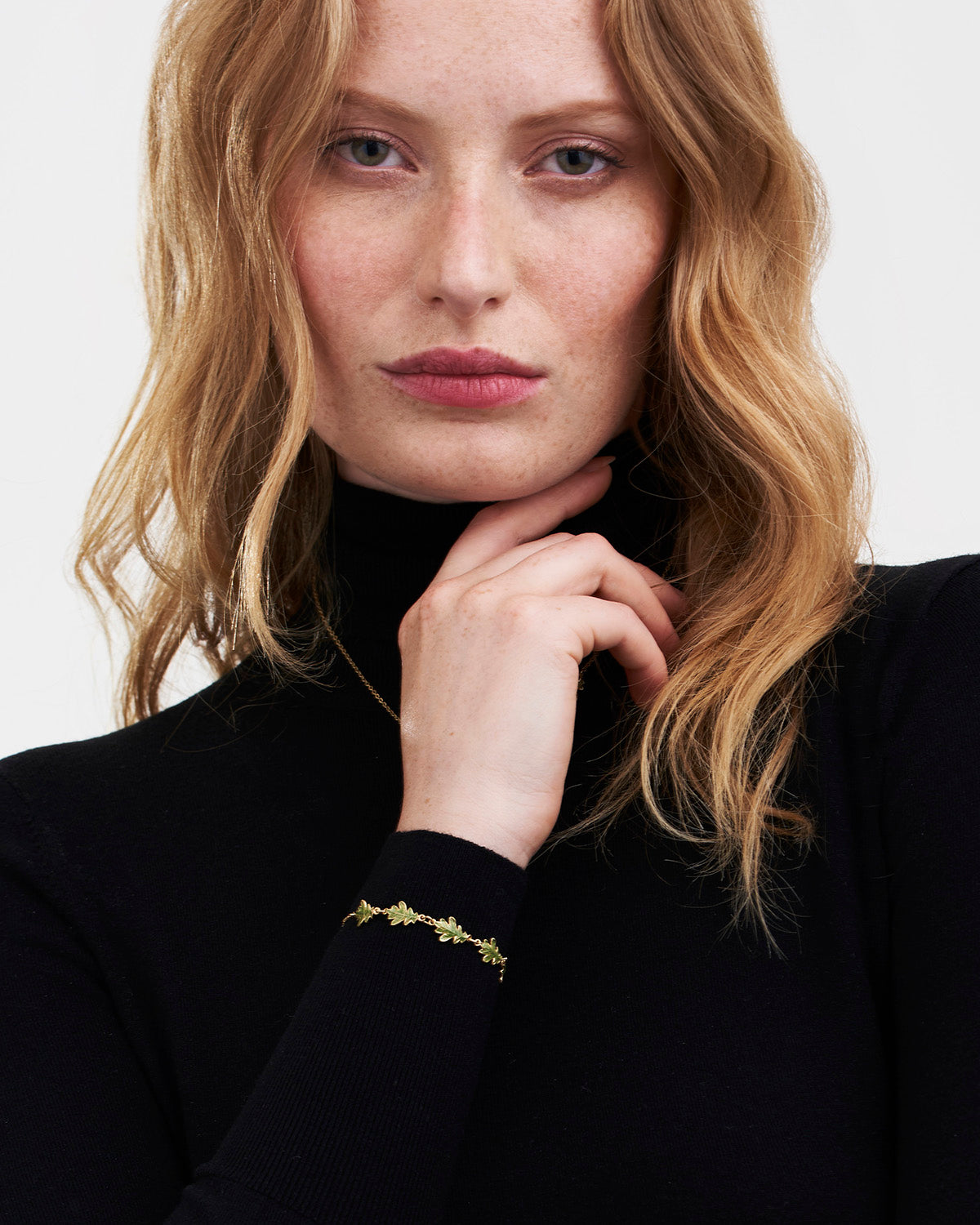 Woman wearing a black turtleneck and gold bracelet with a plain background