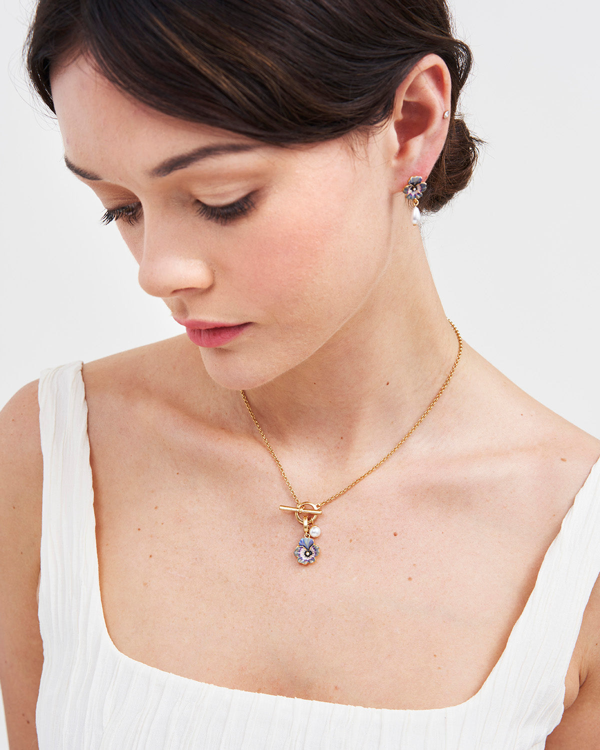 model wearing gold pansy pendant toggle chain necklace with white top on white background