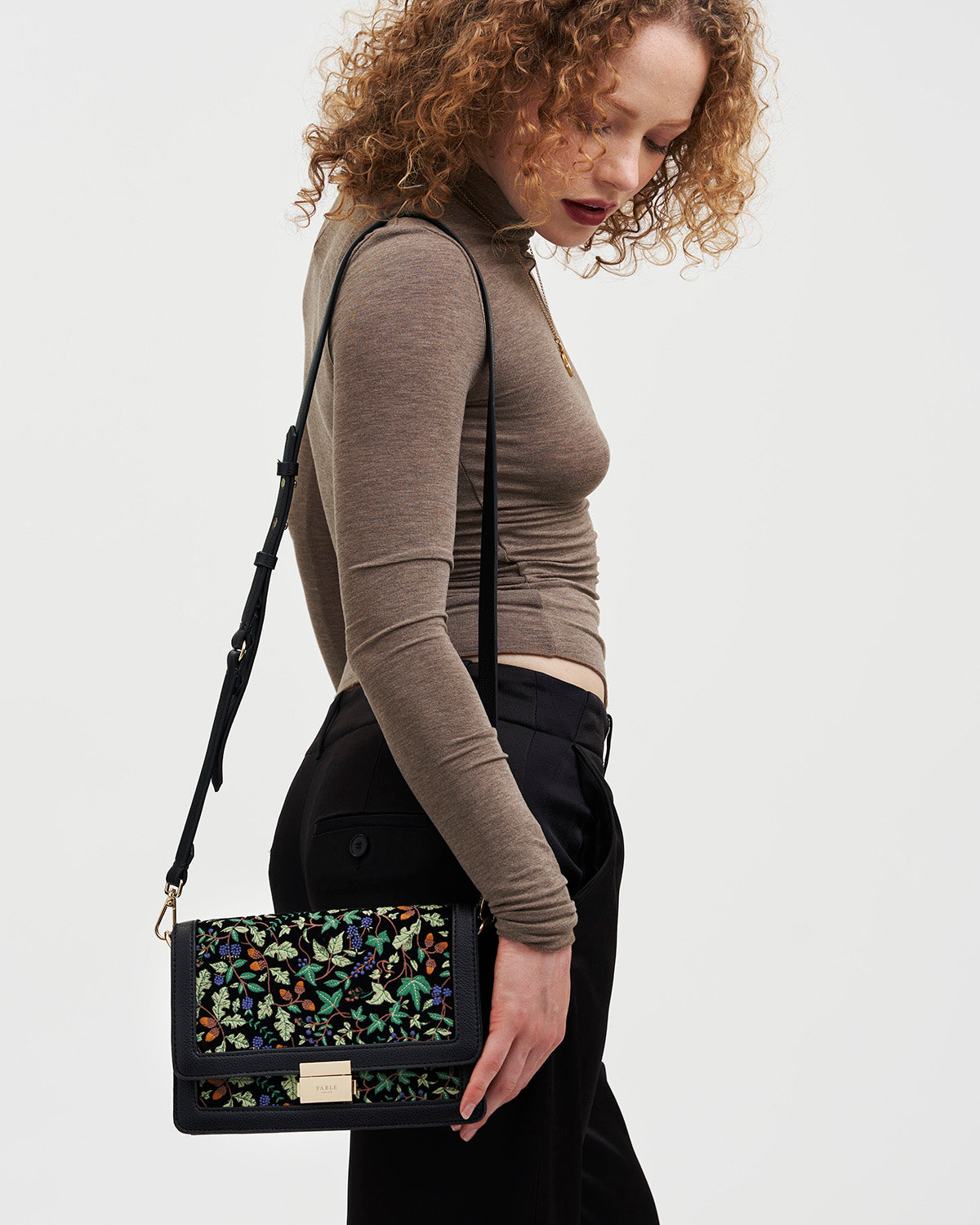 Woman holding a black handbag with oak leaf pattern against a white background