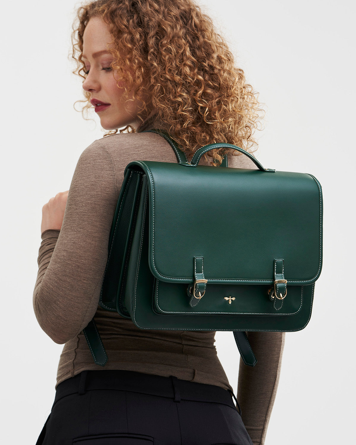 Woman wearing a green satchel backpack against a plain background