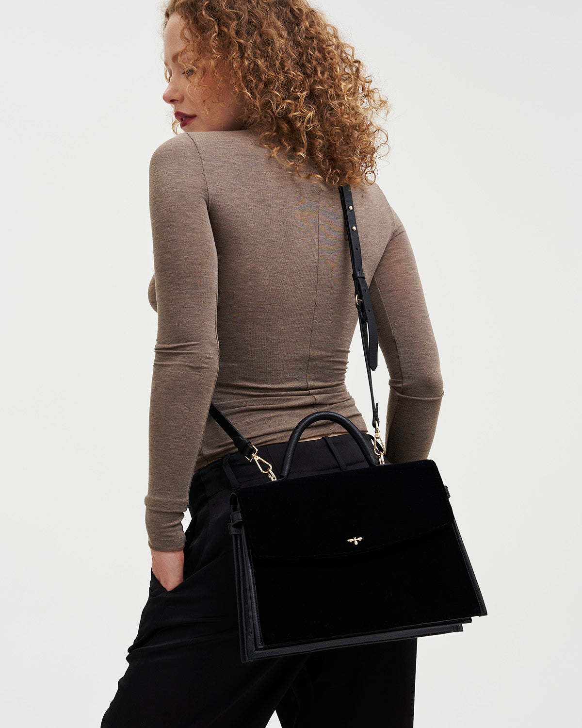 Woman carrying a black velvet handbag on a plain background