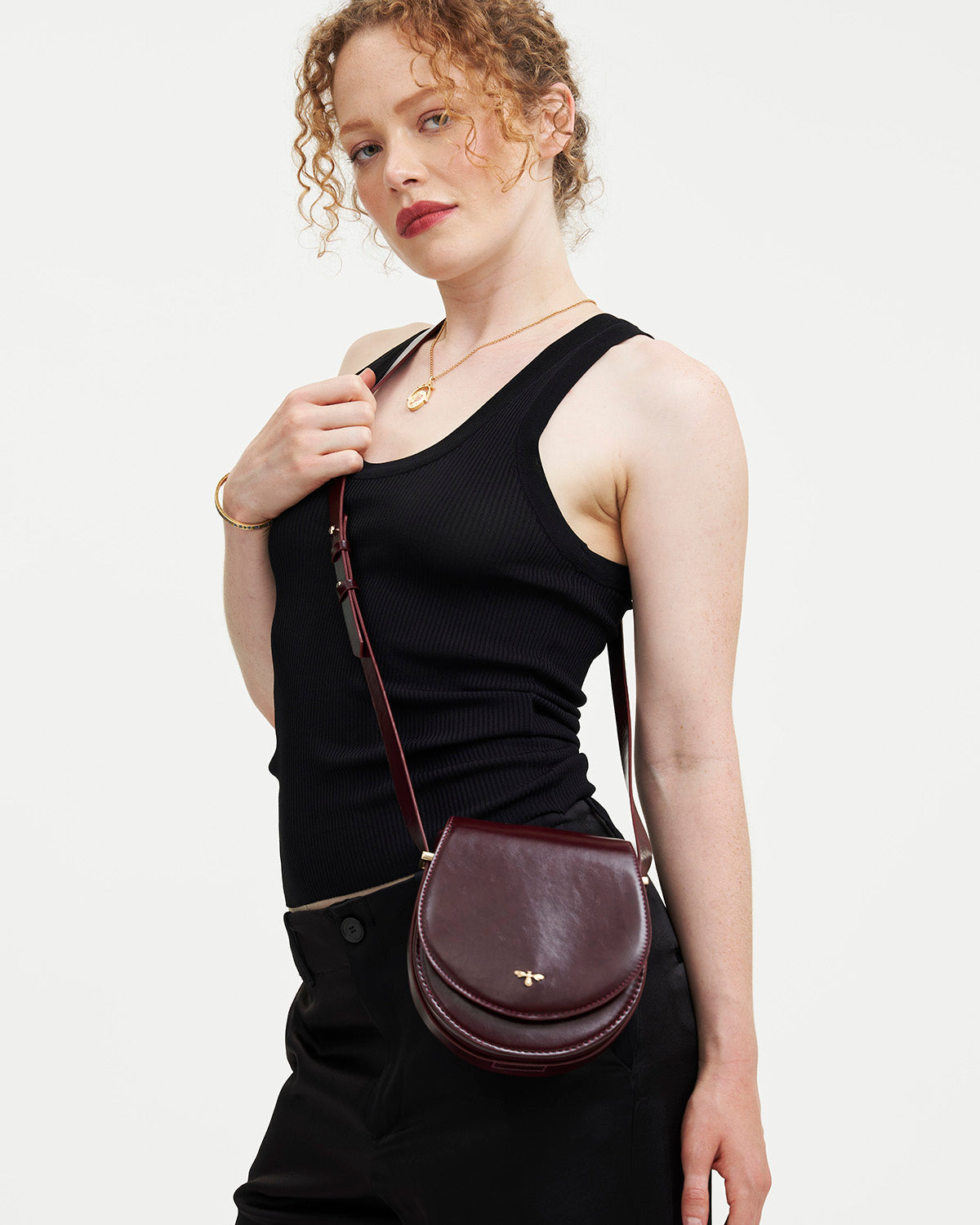 Woman wearing a black sleeveless top and carrying a maroon handbag on a white background