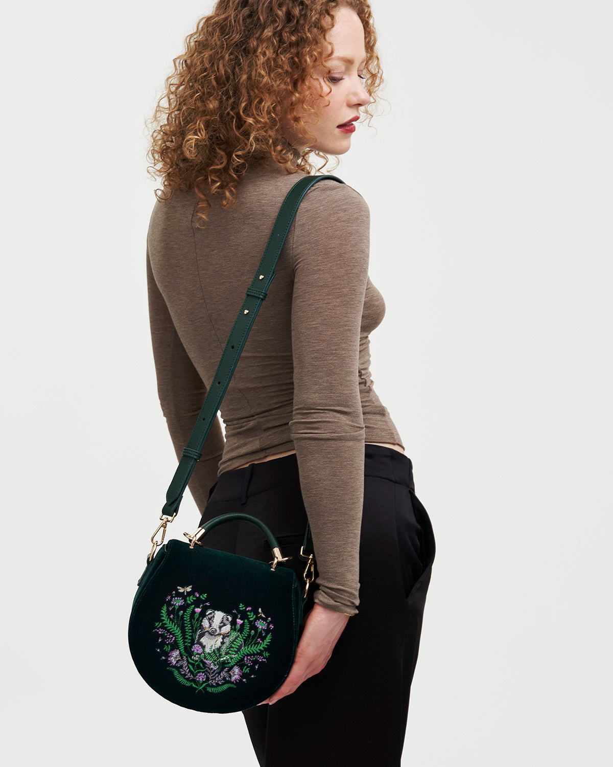 Woman holding a green handbag with floral and badger embroidery on a plain background