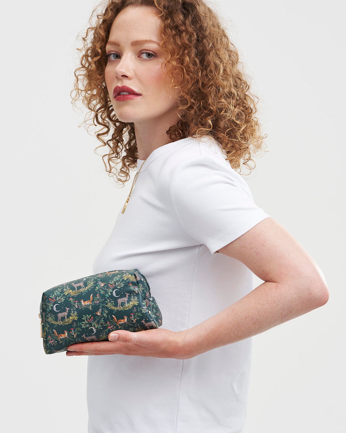 Woman holding a woodland patterned cosmetic bag against a plain background