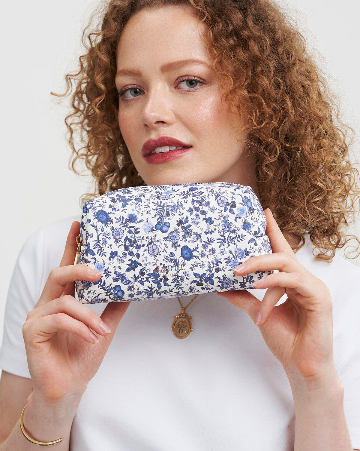 Woman holding a blue floral pouch against a white background