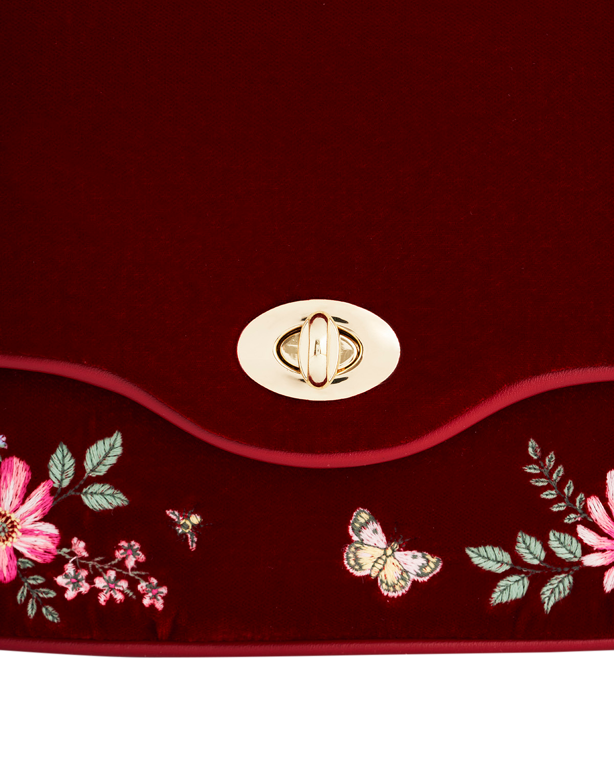 Close-up of a red handbag with floral embroidery and a gold clasp on a matching red background.