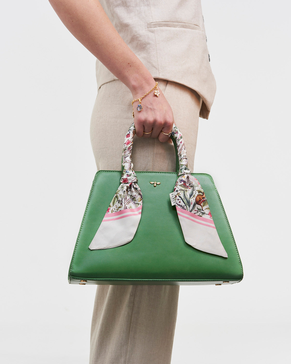 Green handbag with scarf wrapped around handle, held by a person wearing a beige outfit.