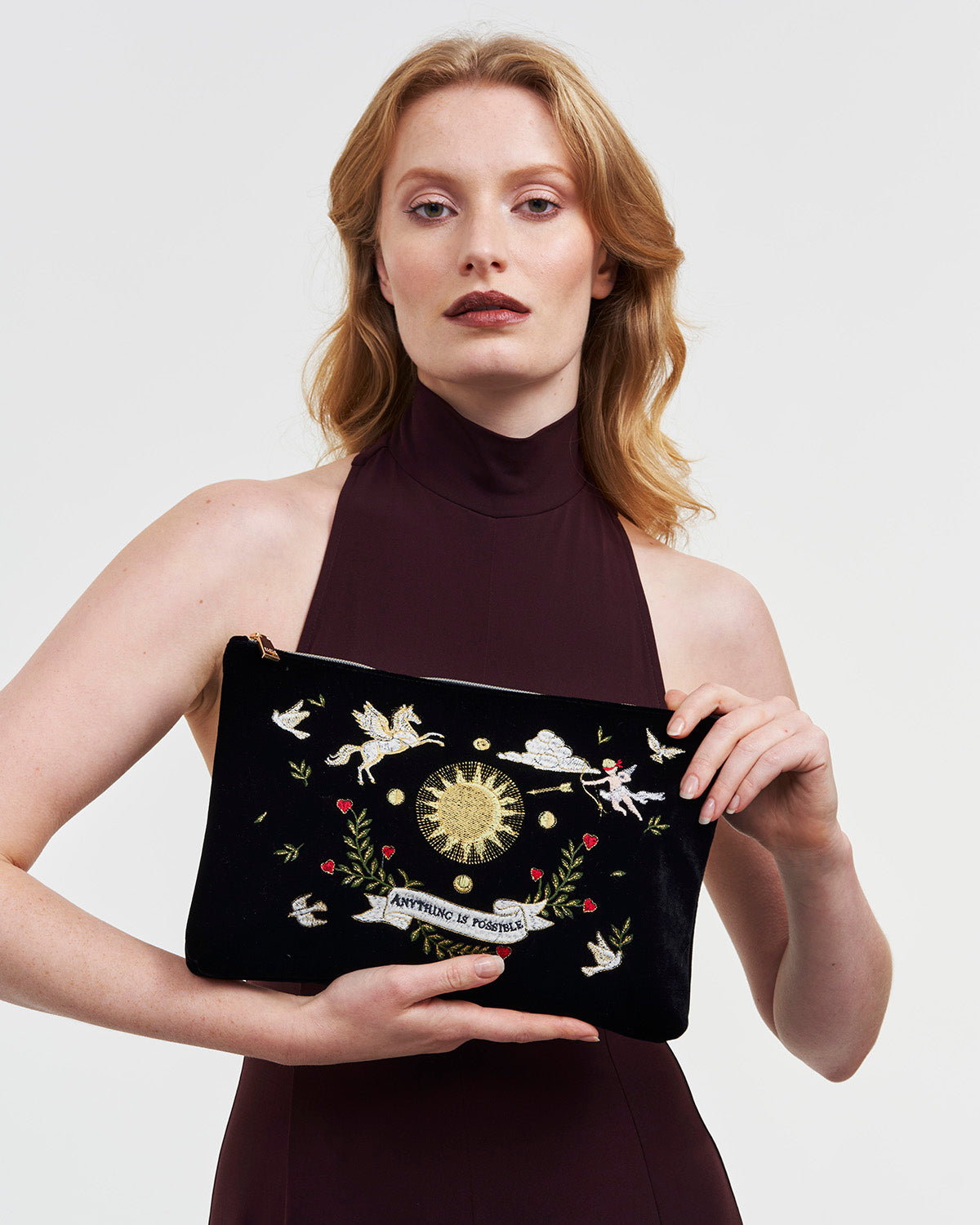 Woman holding a black velvet pouch with embroidered designs against a plain background
