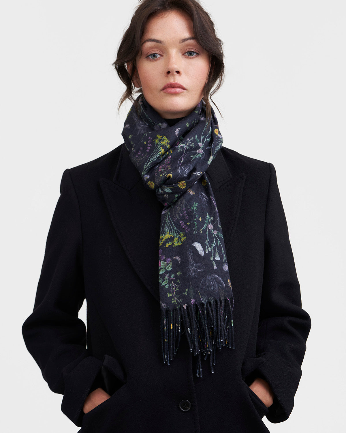 Woman wearing a dark coat and a patterned scarf on a white background