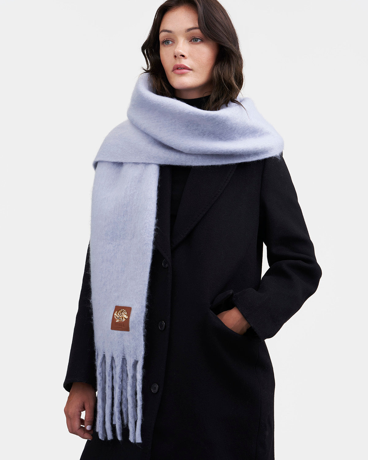 Woman wearing a light blue scarf and black coat on a white background