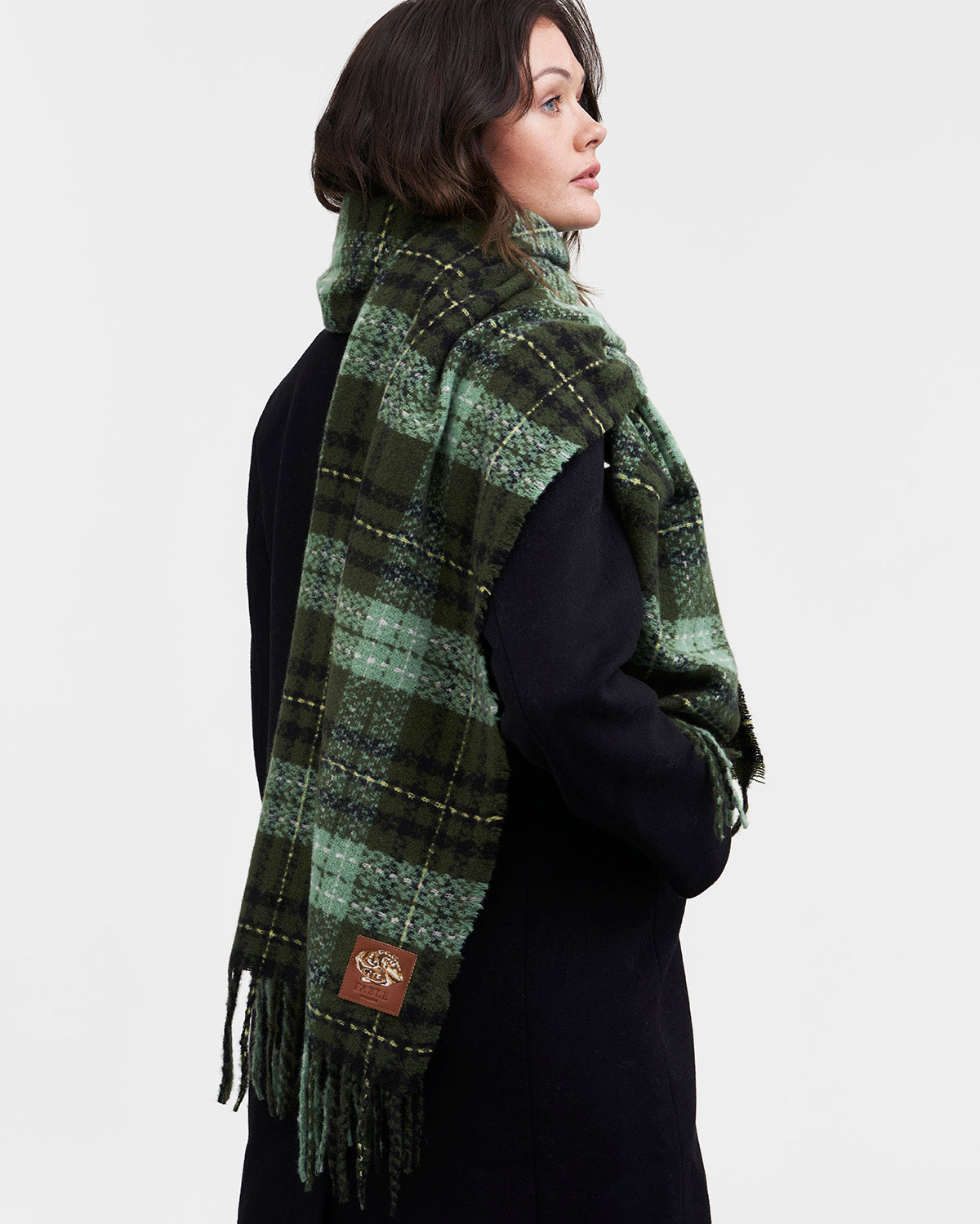 Woman wearing a green plaid scarf with a visible brand logo on a white background