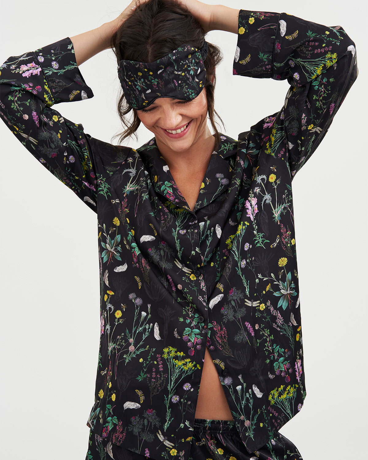 Woman wearing a black floral pajama set with matching sleep mask on a white background