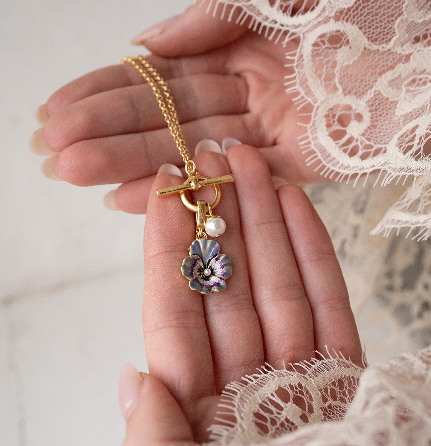 Gold necklace with a floral pendant held in a hand against a lace background