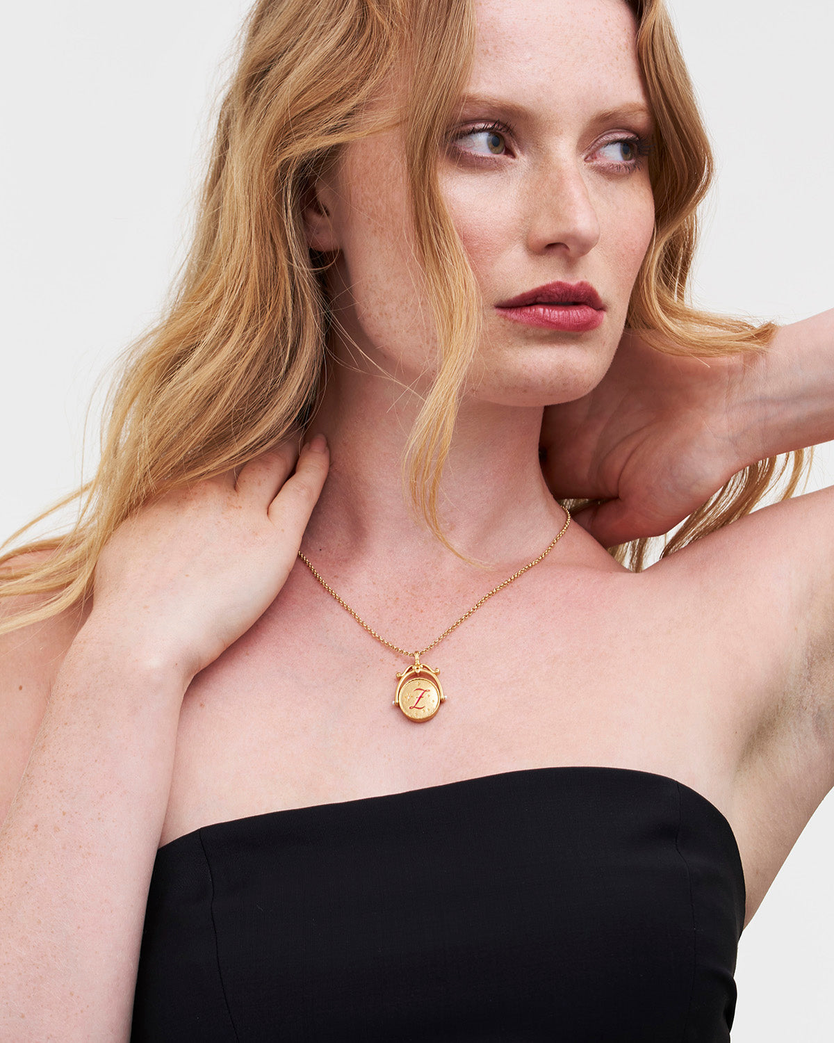 Woman wearing a gold necklace with a pendant against a plain background