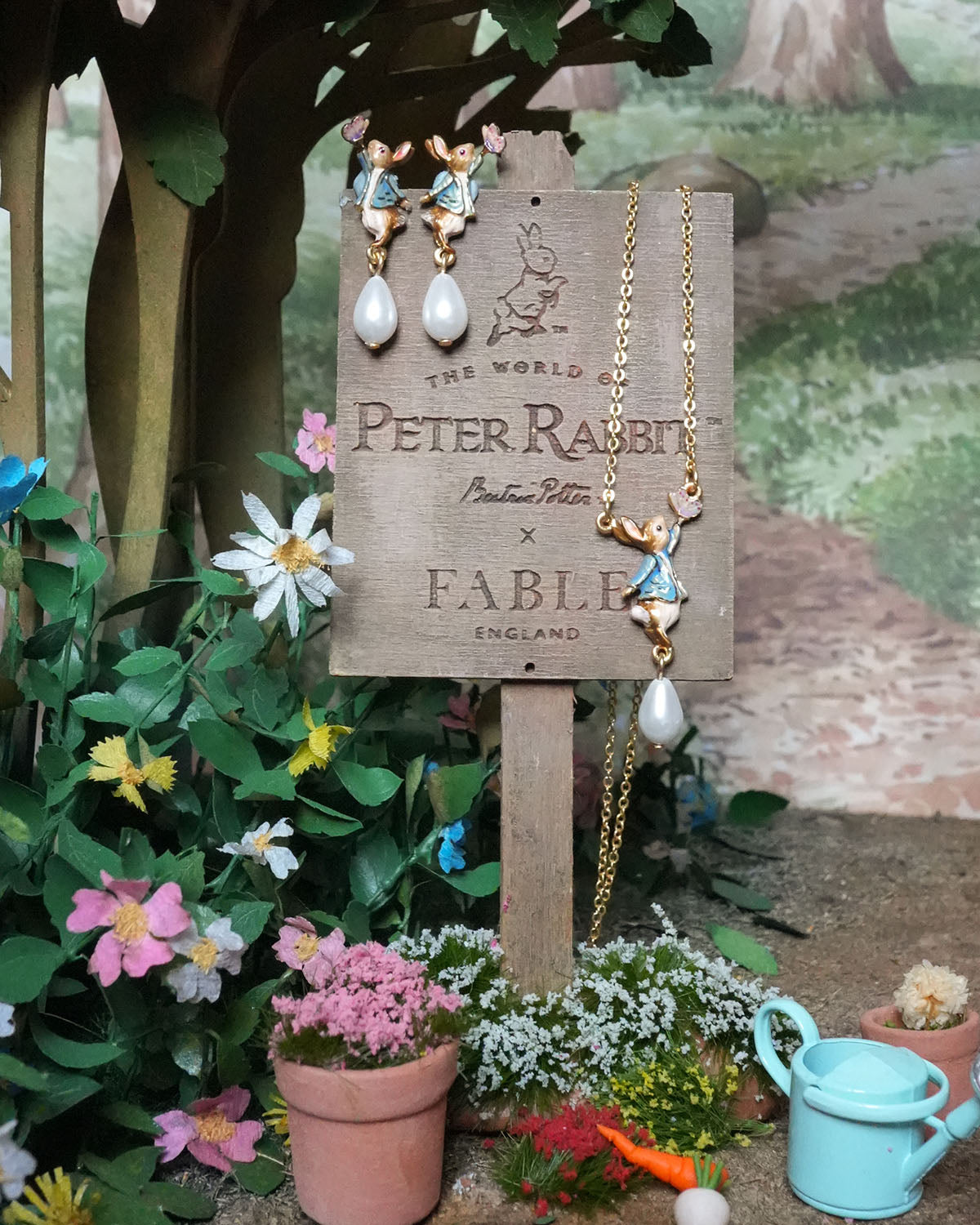 Jewelry set with earrings and necklace on a 'Peter Rabbit' branded stand in a garden setting.