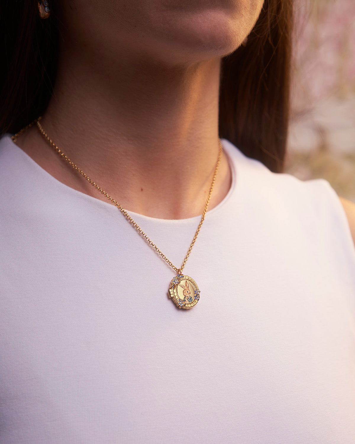 Gold necklace with a pendant worn by a person against a blurred background