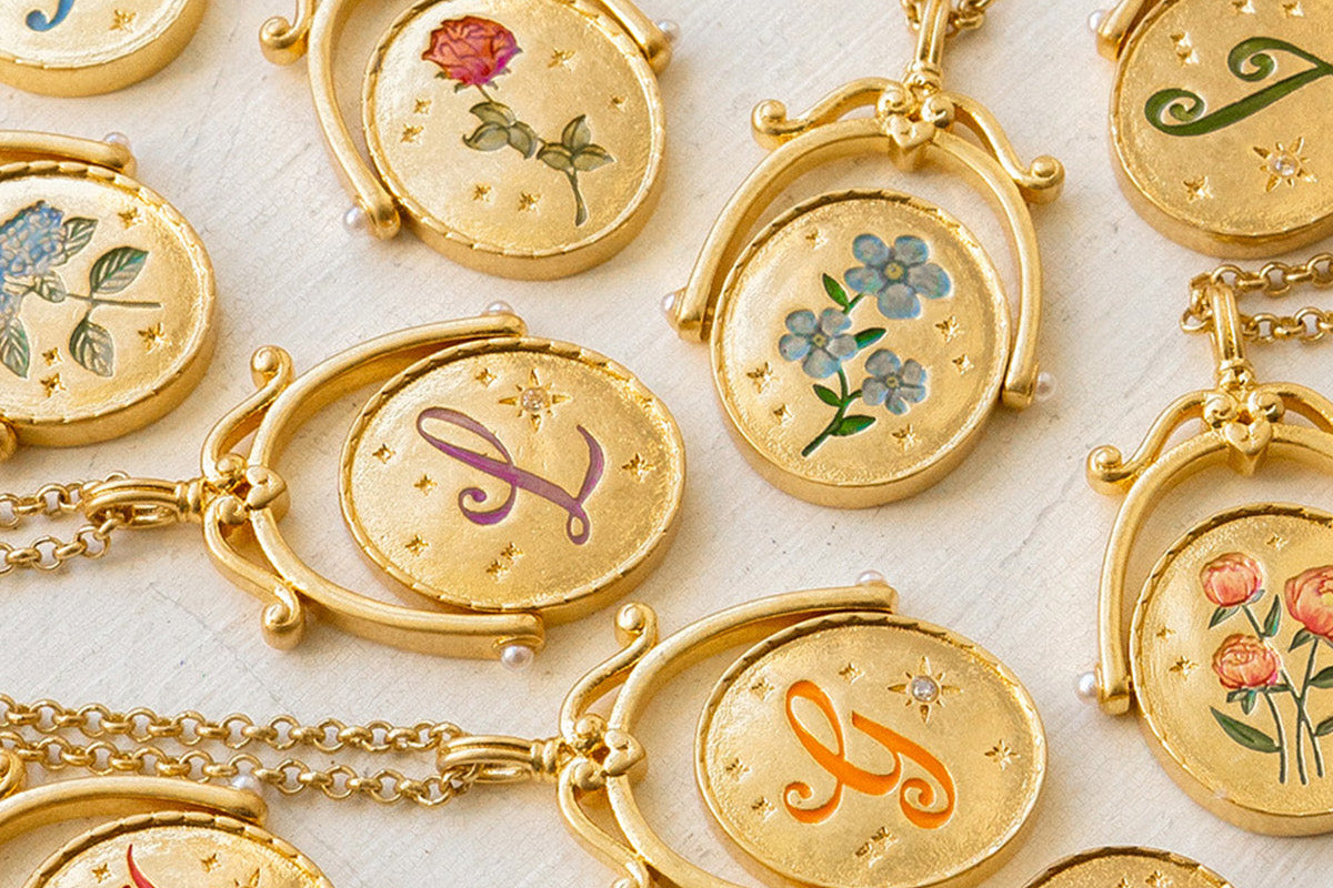Gold necklaces with circular pendants featuring letters and floral designs on a light background