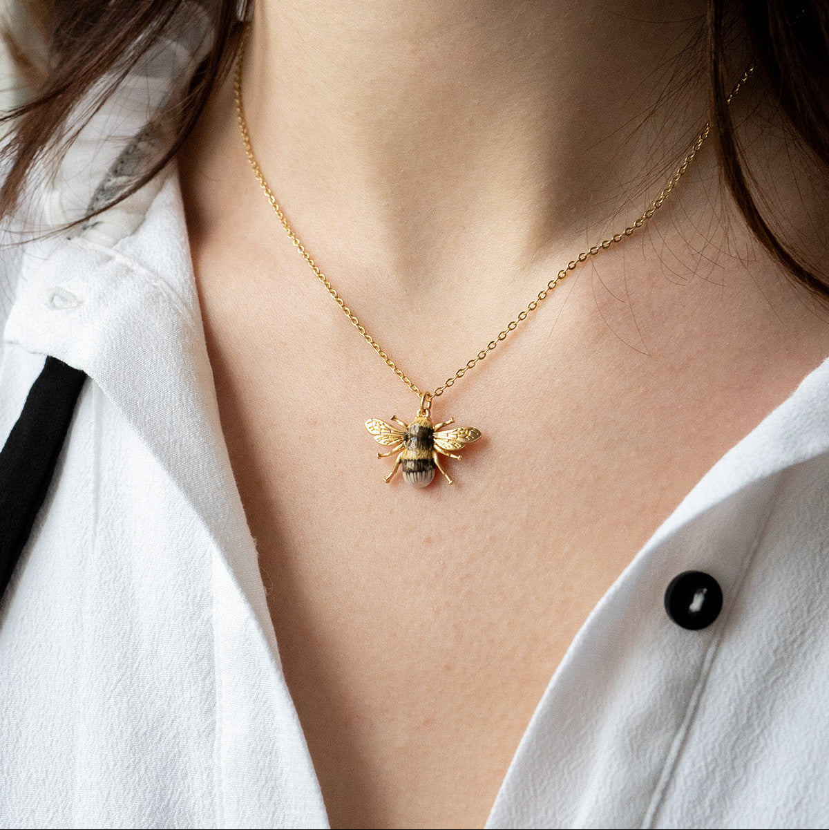 Gold bee necklace on a woman wearing a white shirt with black buttons.