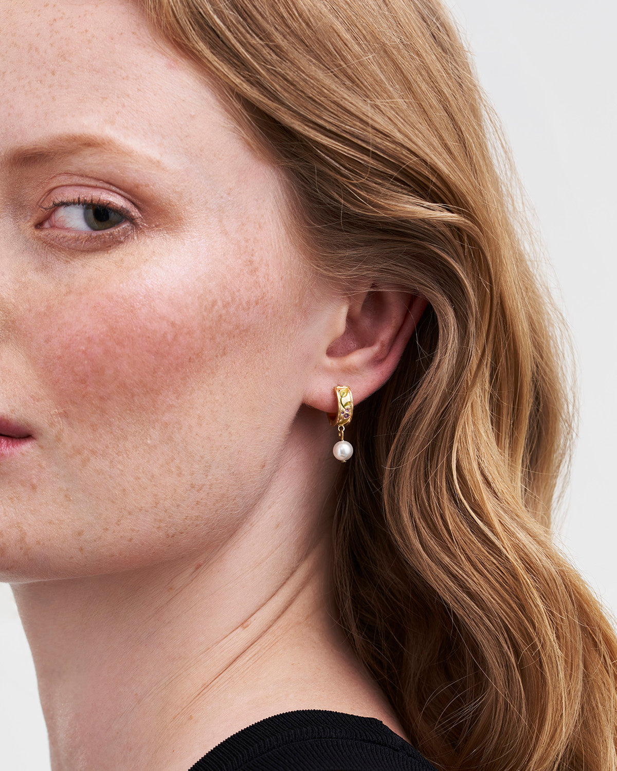 Close-up of a person wearing a gold earring with a pearl on a plain background