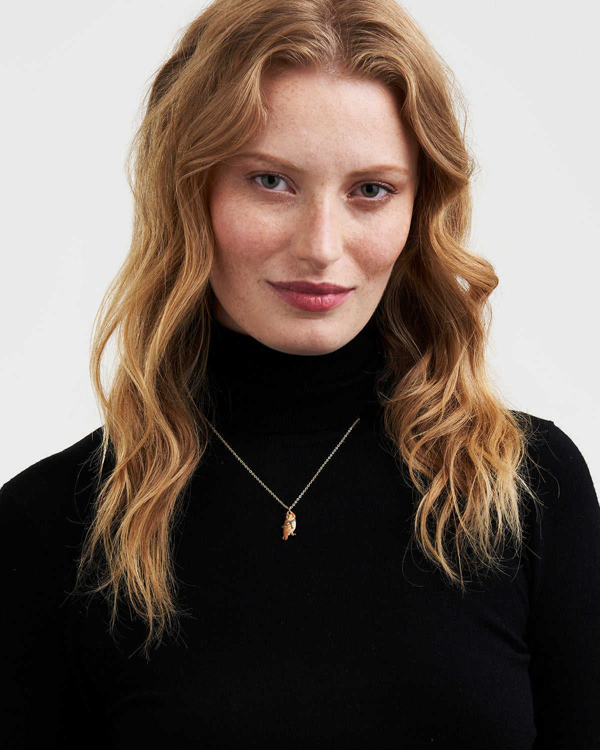 Woman wearing a black turtleneck and gold necklace against a white background