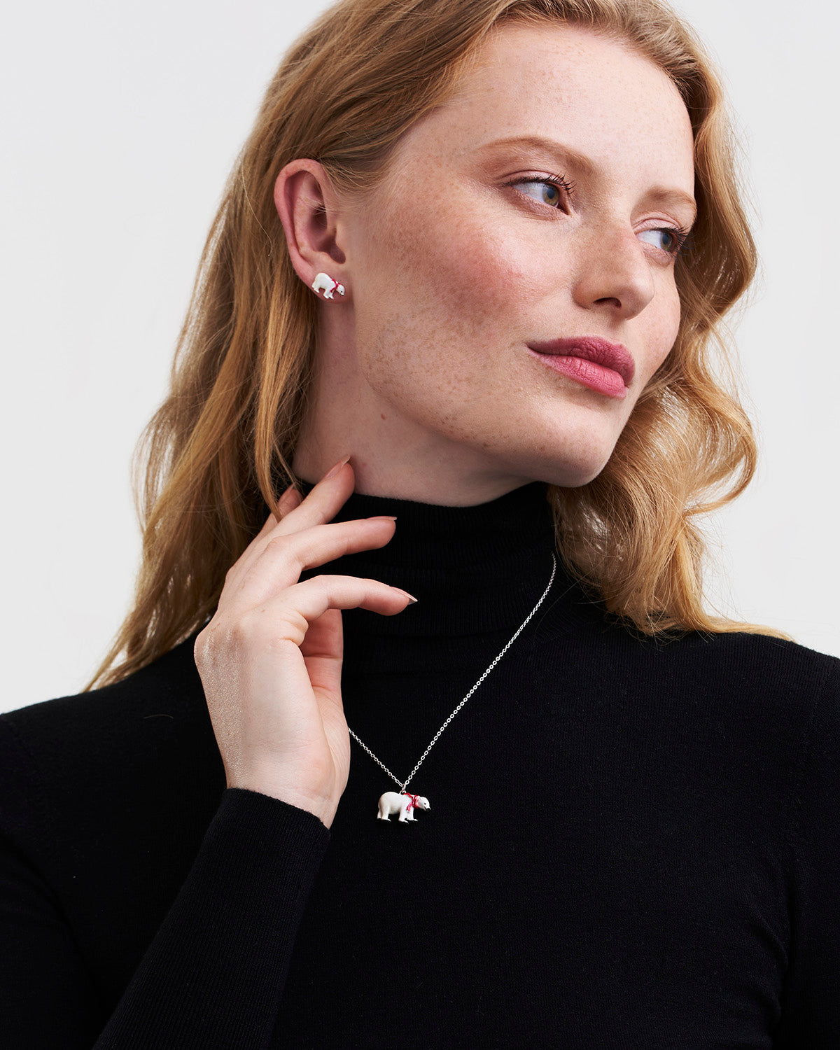 Woman wearing a black turtleneck and silver necklace with a small pendant, against a plain background.