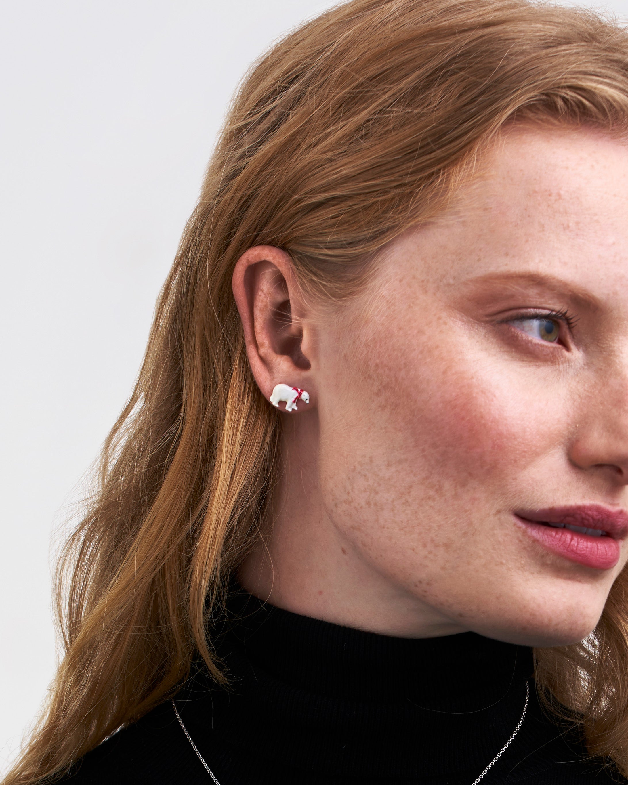 Close-up of a woman wearing polar bear earrings with a plain background