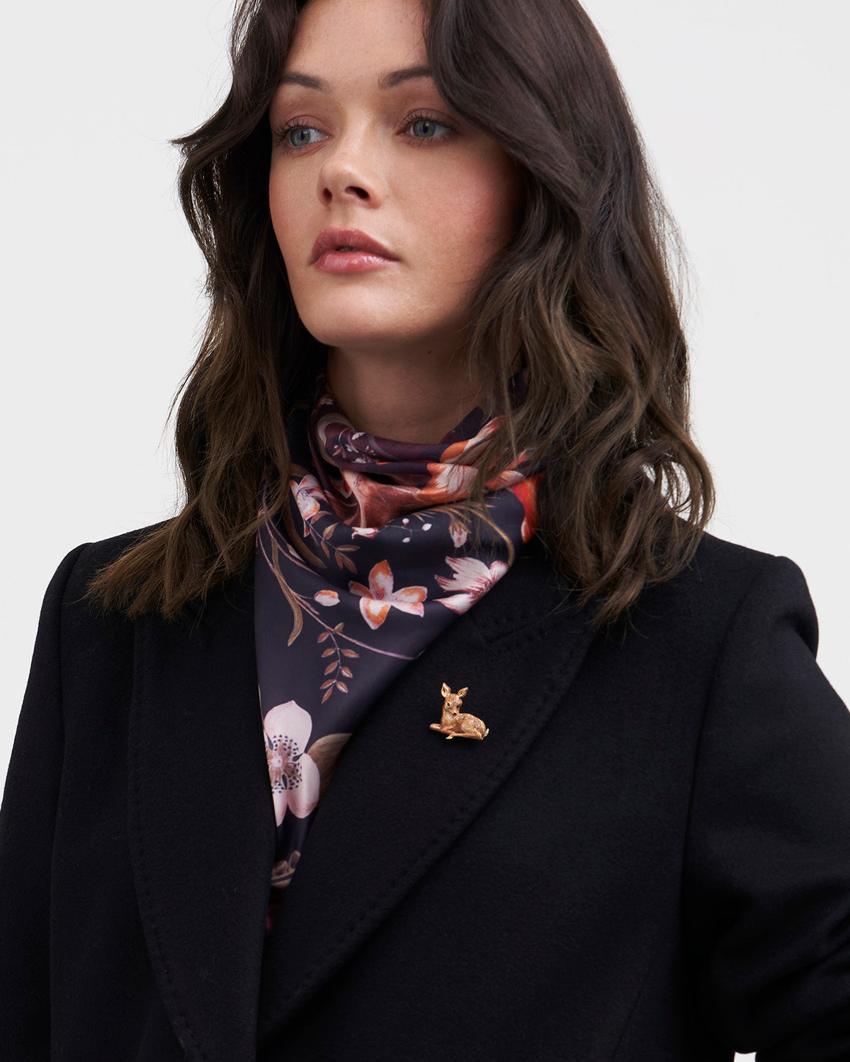 Woman wearing a floral scarf and fawn enamel brooch on black blazer on a white background