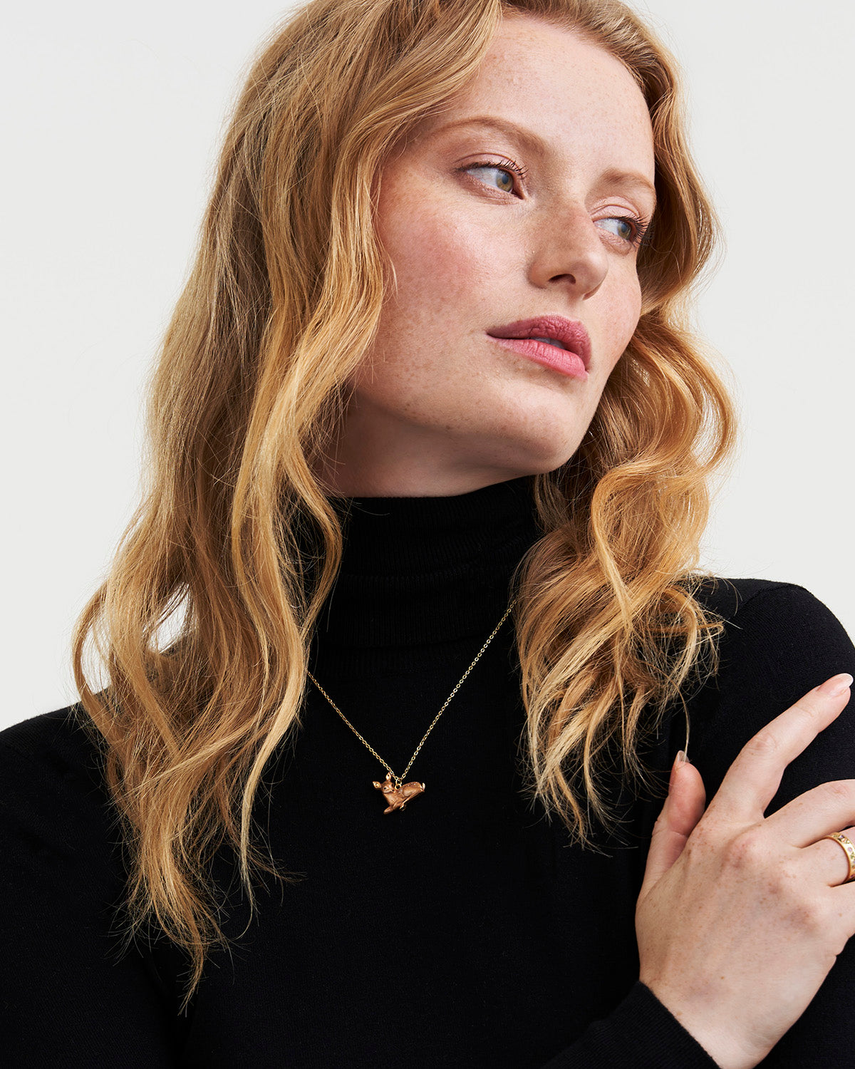 Woman wearing a black turtleneck and gold necklace with a small pendant against a light background