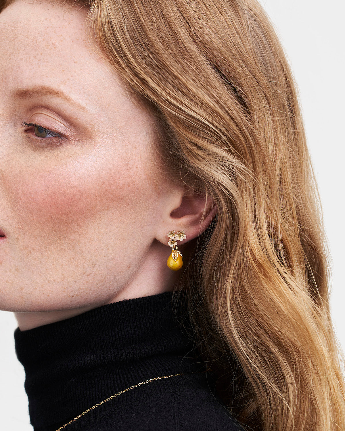 Close-up of a woman wearing a gold earring with a yellow gemstone on a plain background