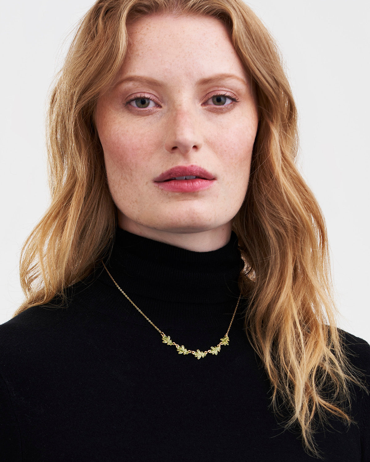 Woman wearing a gold necklace against a plain background