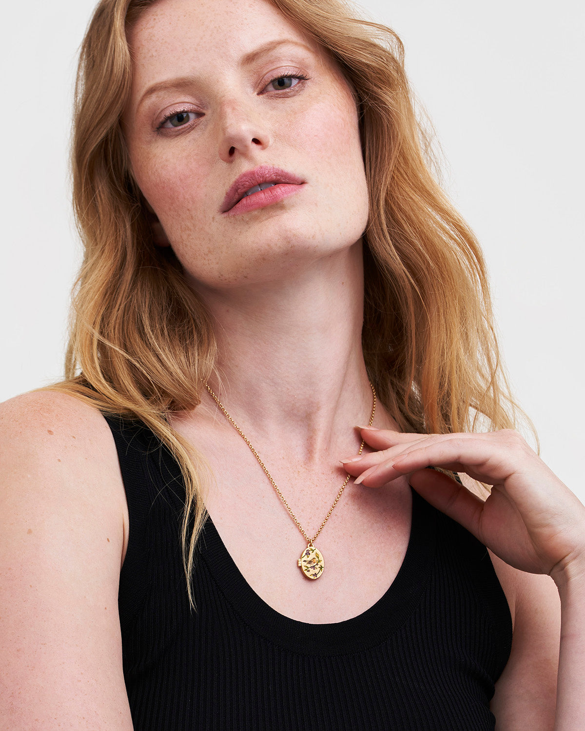 Woman wearing a gold robin locket necklace with a black top against a plain background