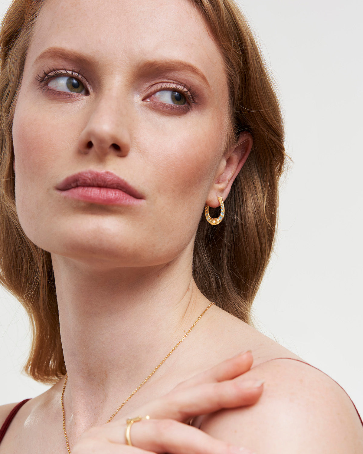 Woman wearing gold jewelry including earrings, necklace, and ring on a plain background