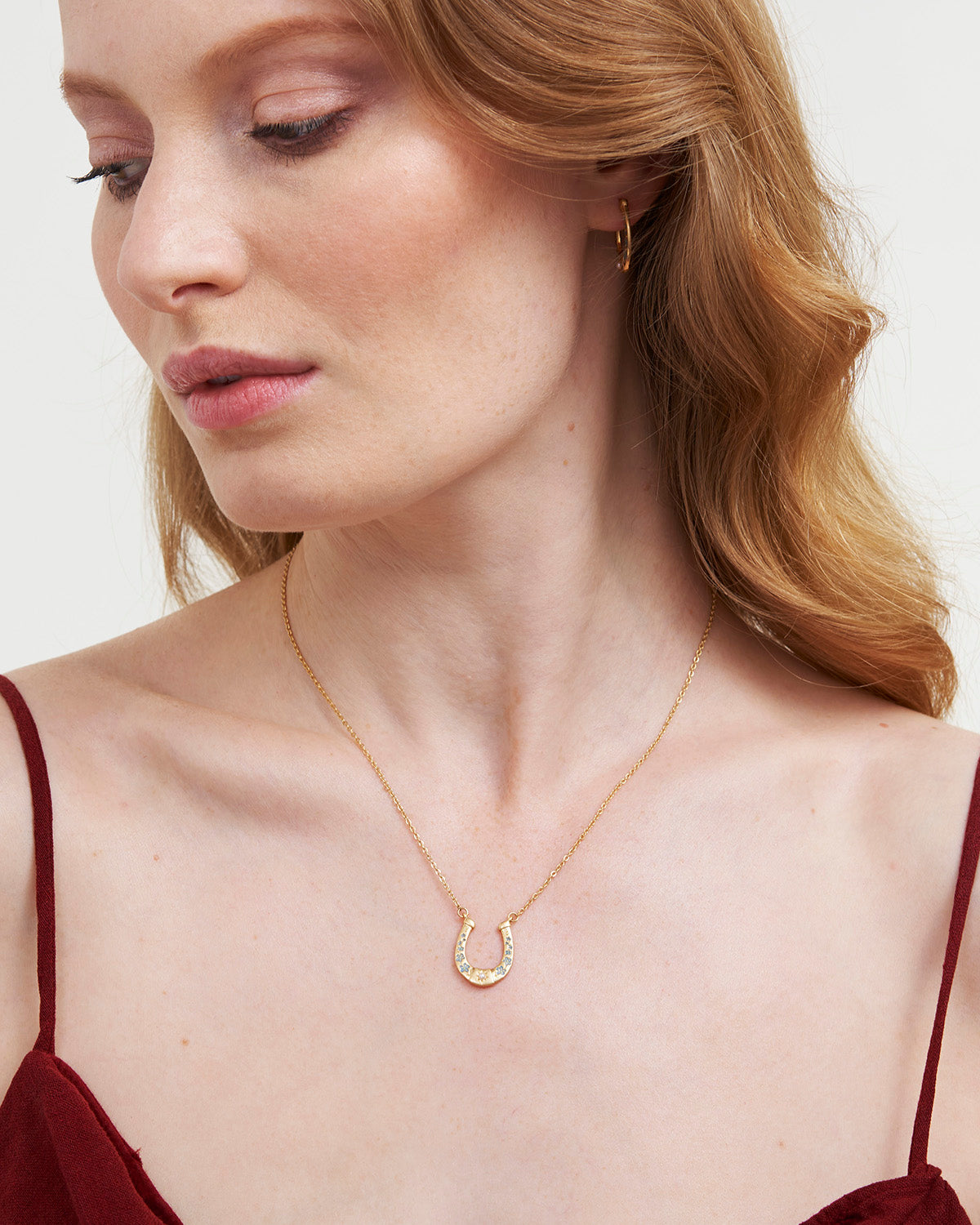 Woman wearing a gold necklace with a horseshoe pendant on a plain background