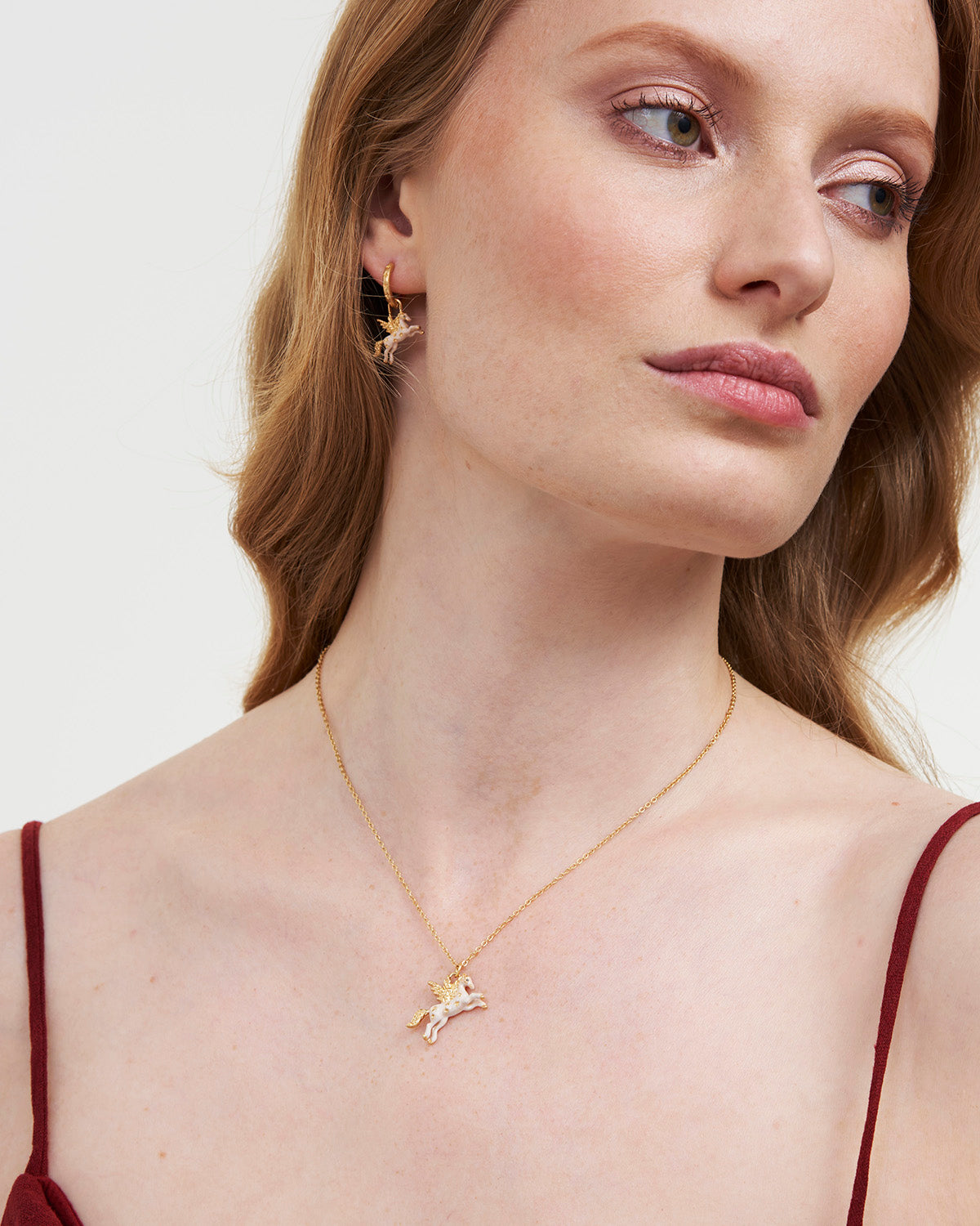 Woman wearing a gold necklace with a small pendant on a plain background