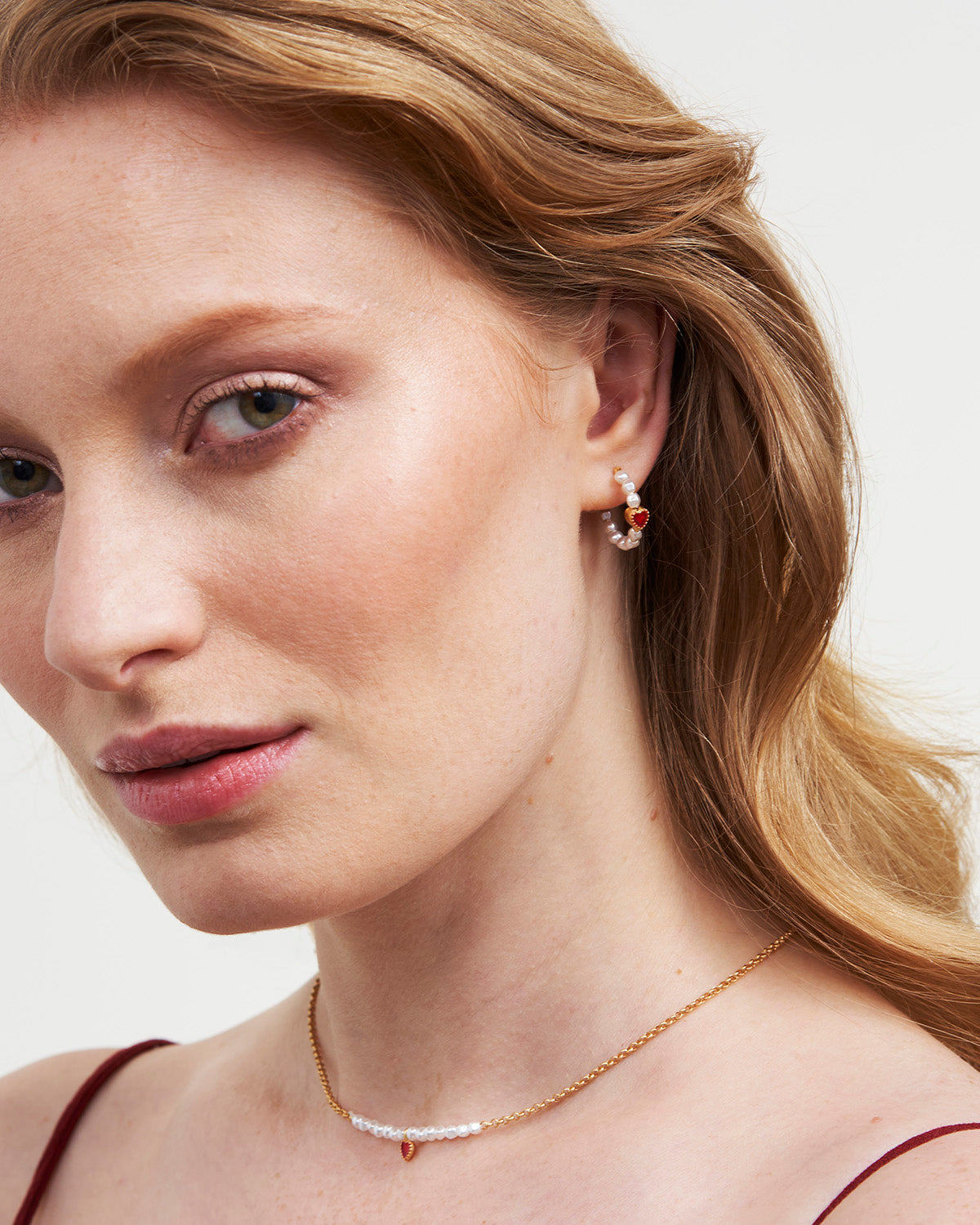 Close-up of a woman wearing a gold necklace and earrings on a plain background
