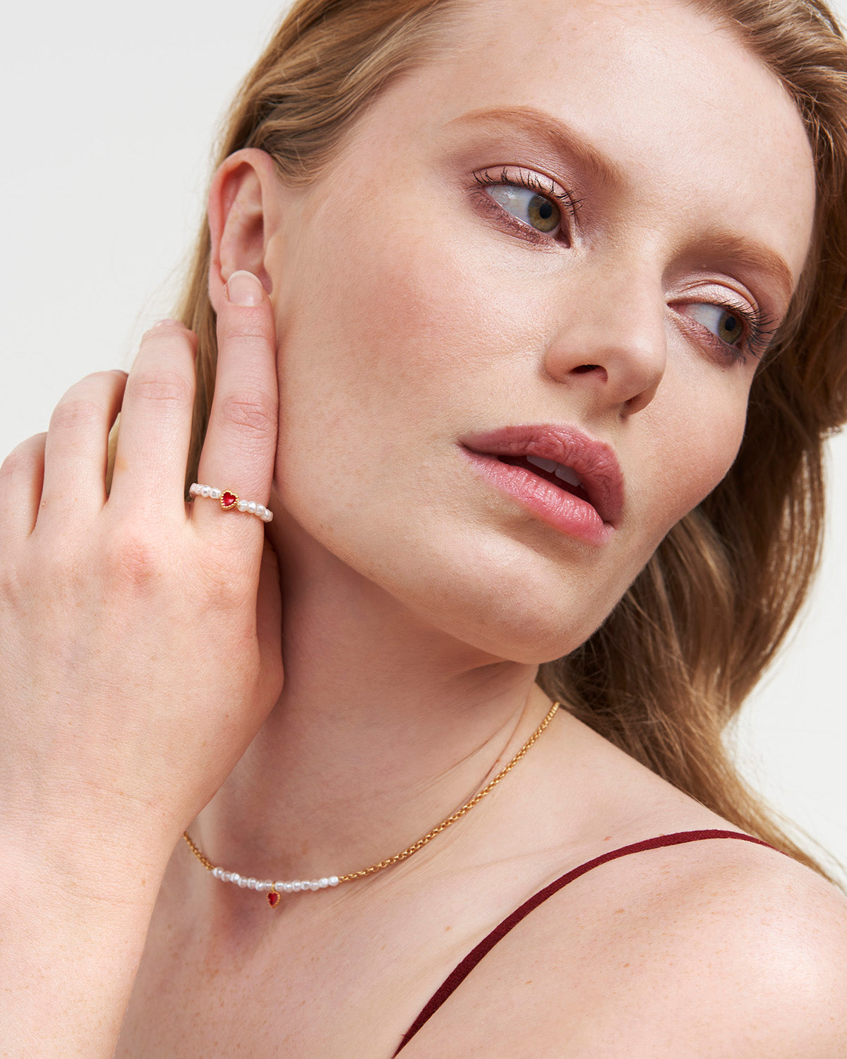Woman wearing a pearl and gold necklace and ring, with a neutral background