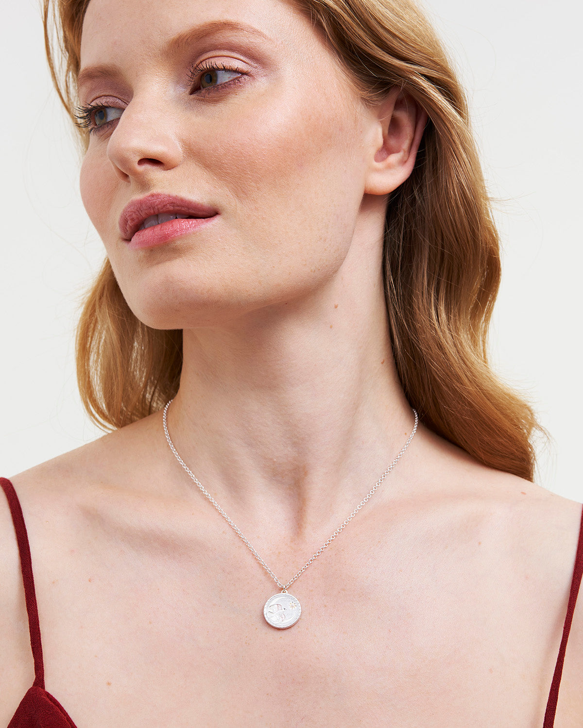 Woman wearing a delicate necklace with a small pendant against a neutral background
