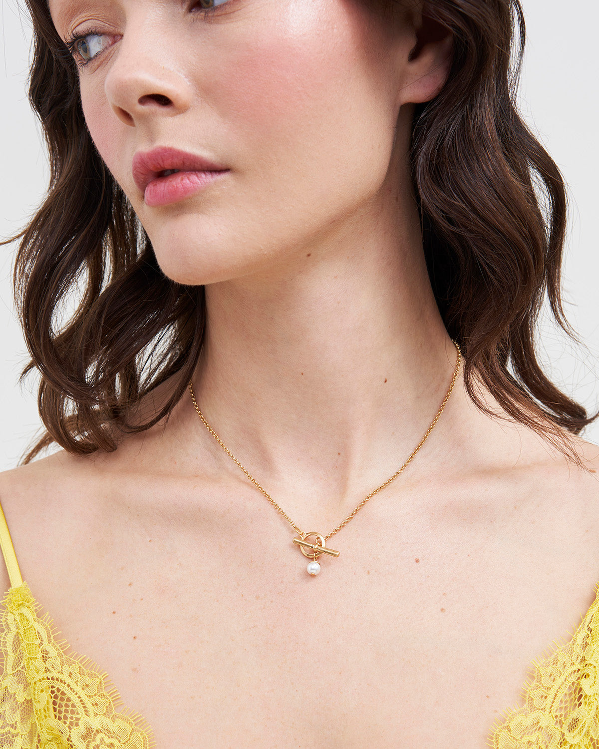 Model wearing gold toggle necklace with pearl on white background