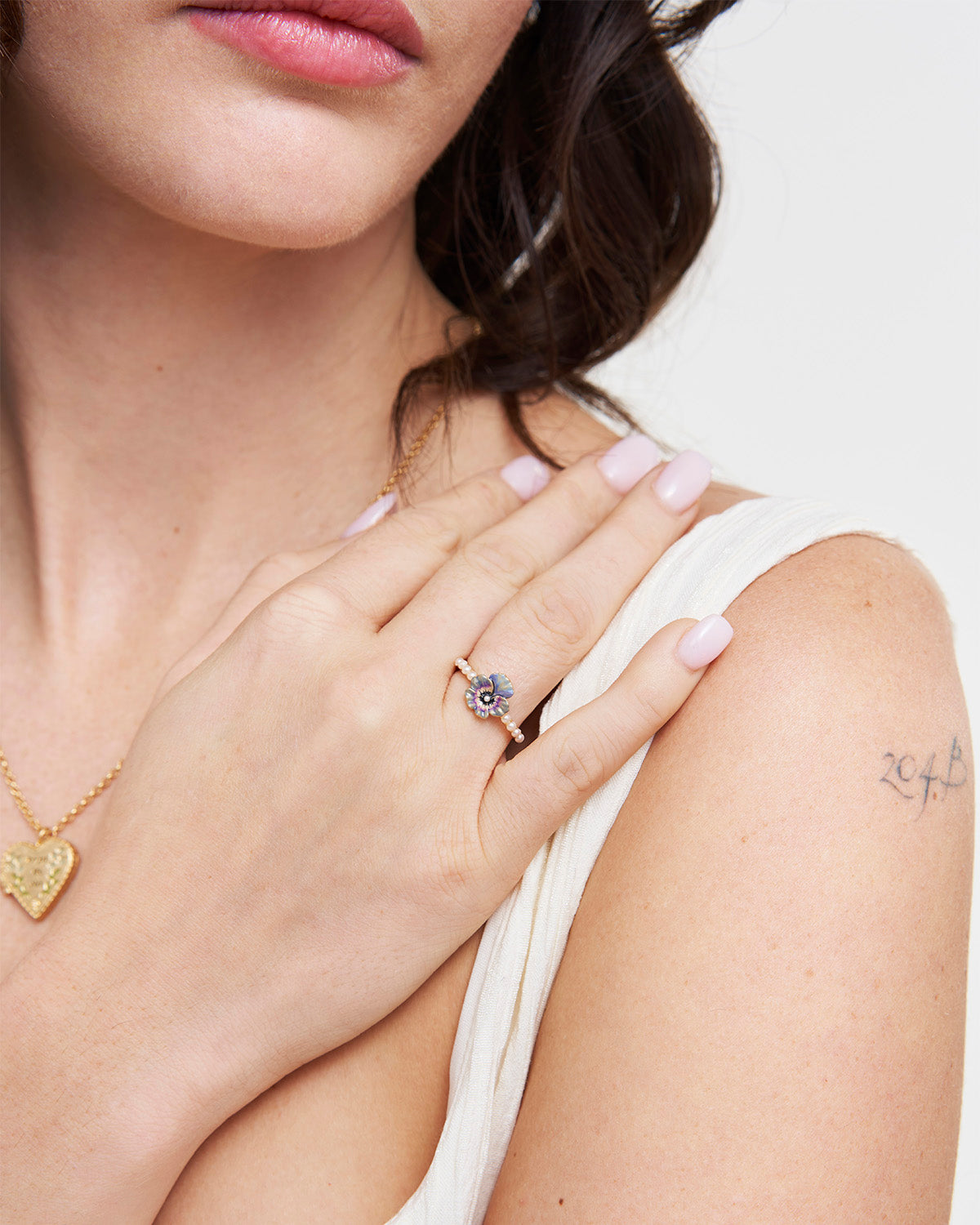 Close-up of a woman's hand wearing a gold ring with a blue enamel pansy detail, with a blurred background.
