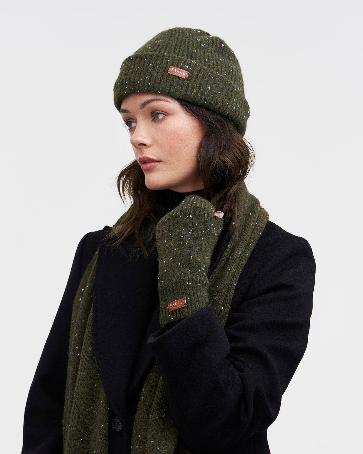 Woman wearing a green knit hat and scarf with a visible brand logo on a white background