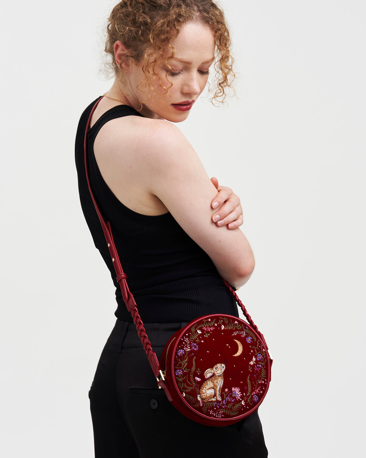 Woman wearing a red embroidered bag with intricate designs on a plain background