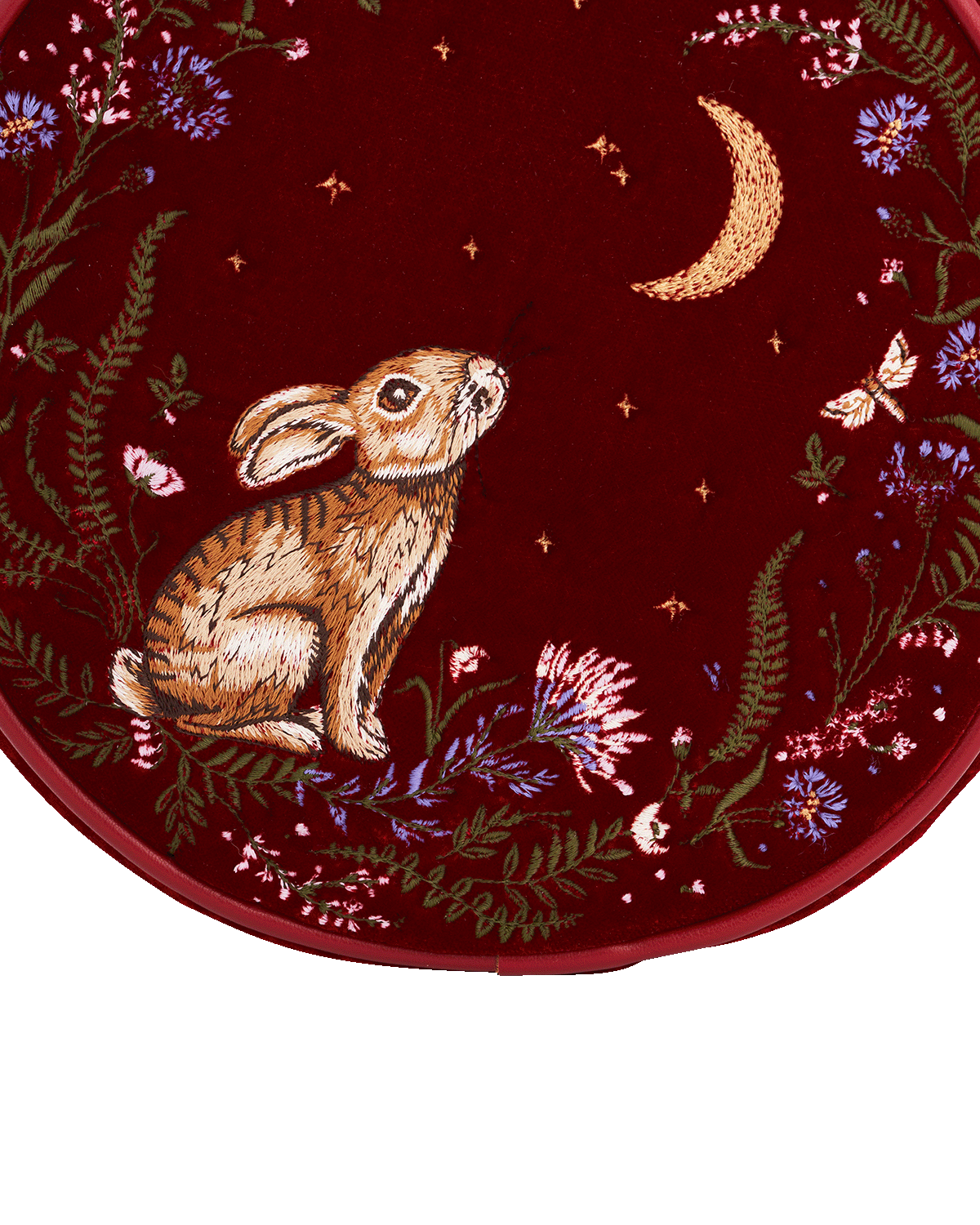 Embroidered design of a rabbit among flowers and a moon on a red background