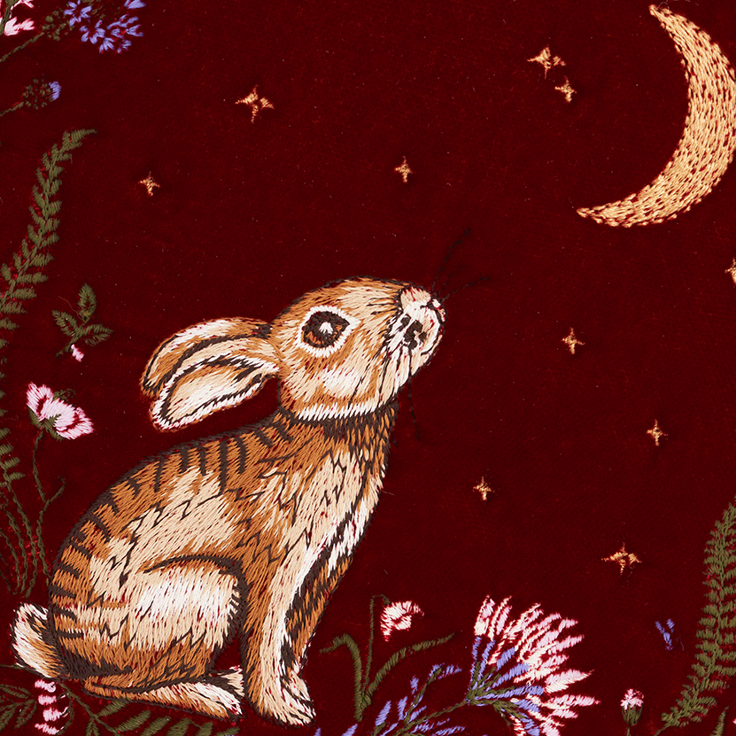 Embroidered design of a rabbit among flowers and a moon on a red background
