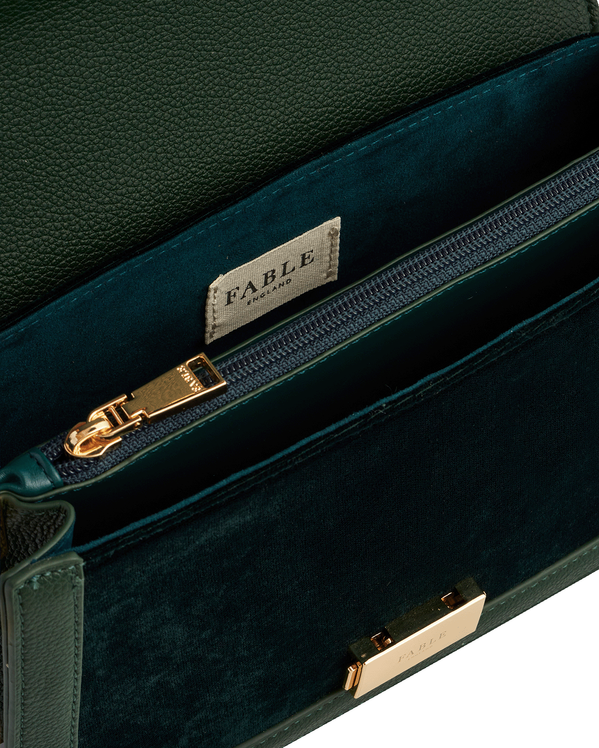 Green velvet clutch bag with gold zipper and 'Fable England' label on a white background