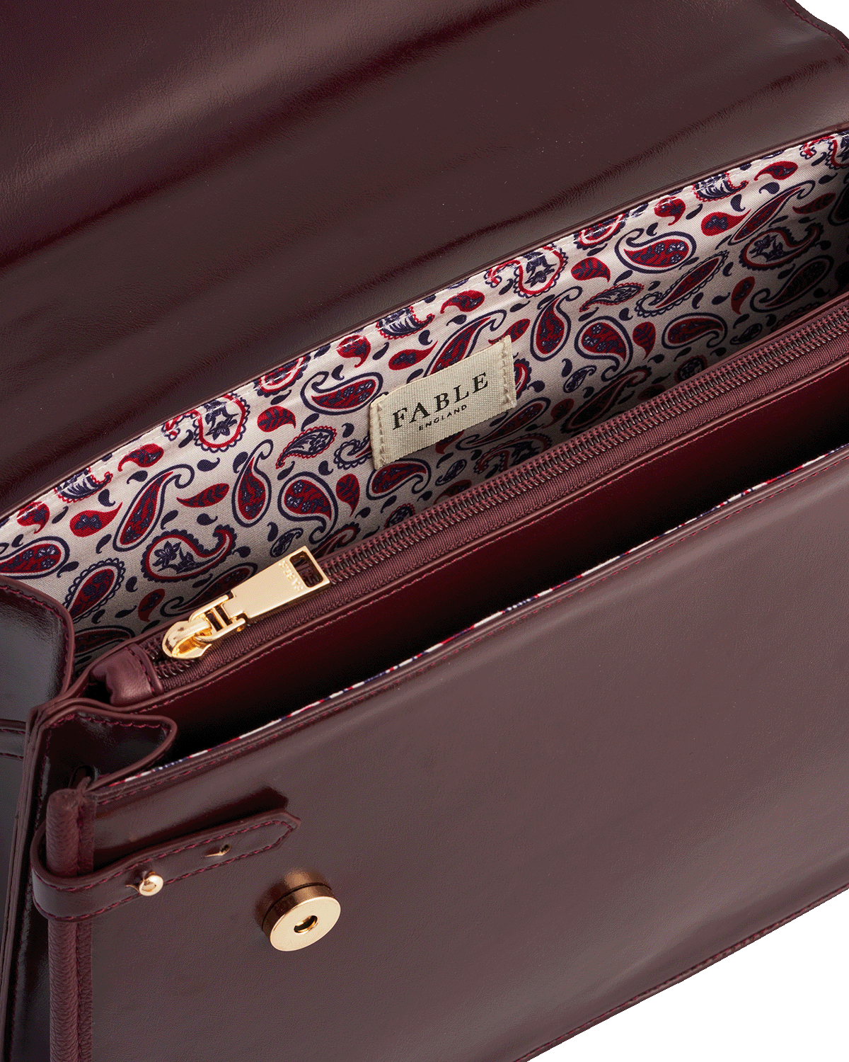 Close-up of a cherry red leather handbag with a patterned handle and 'Fable England' branding.