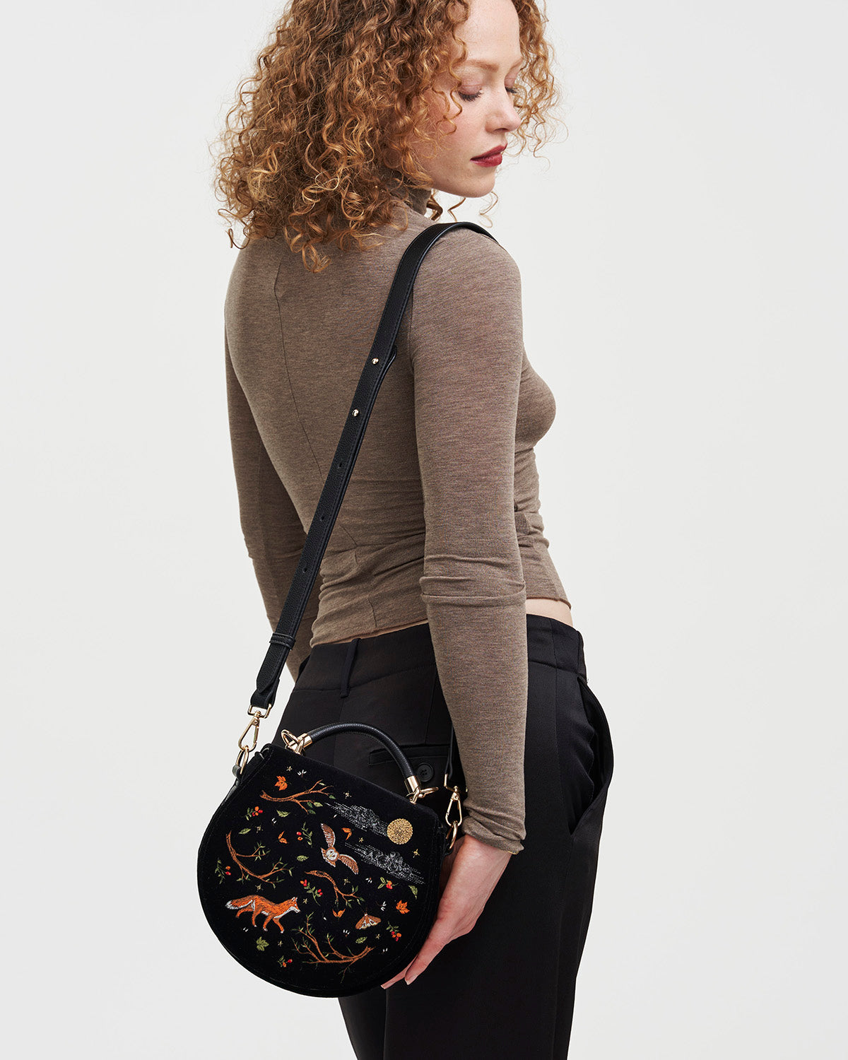 Woman holding a black handbag with intricate designs on a plain background