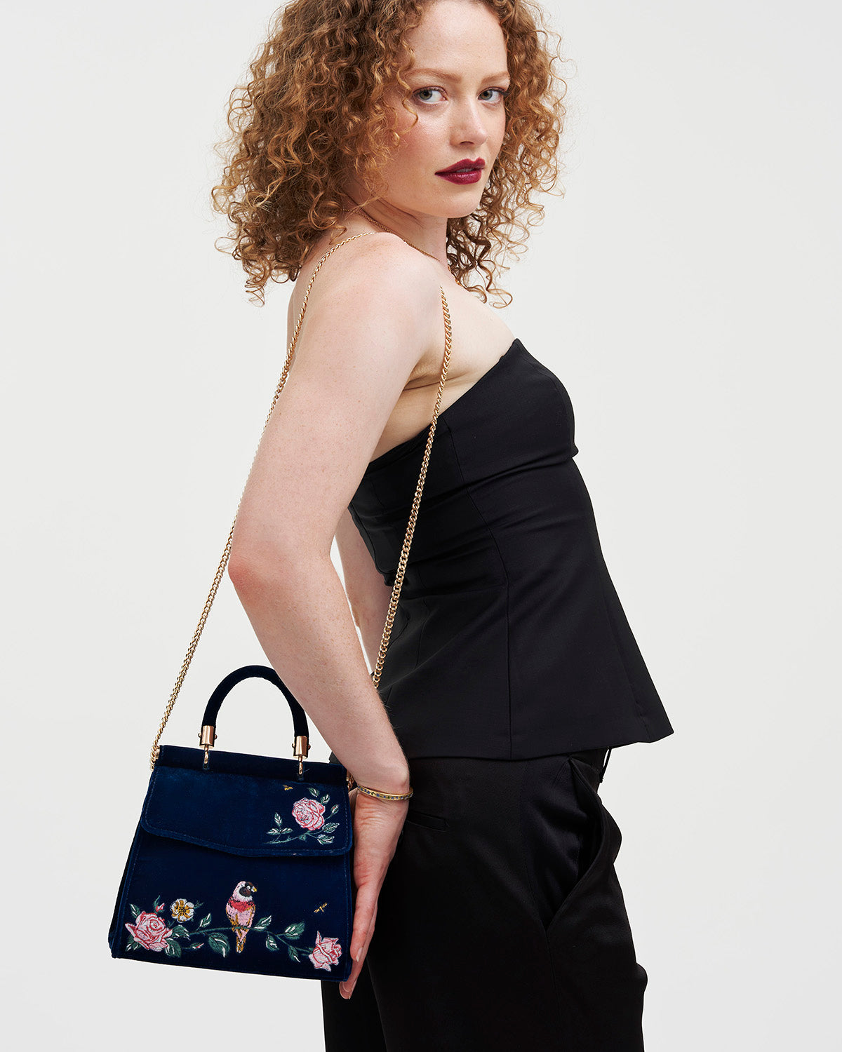 Woman holding a navy handbag with floral embroidery against a white background
